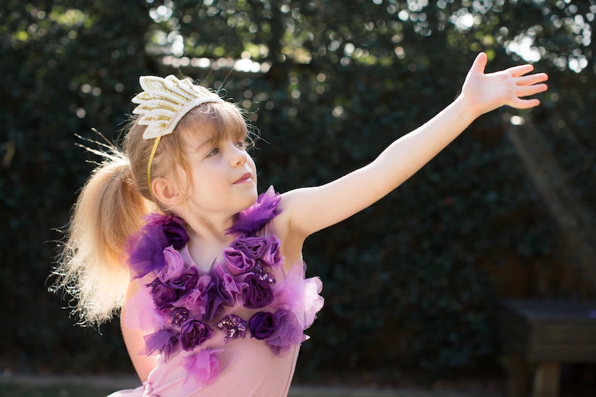 Young girl in a tutu and a tiara dances around a backyard.