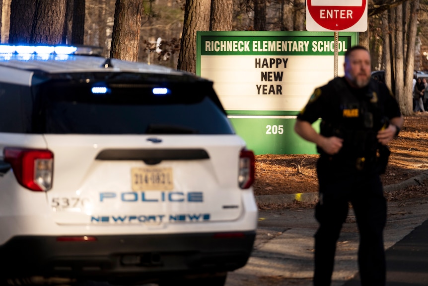 A police officer stands outside a school with Richland Elementary School sign at dusk