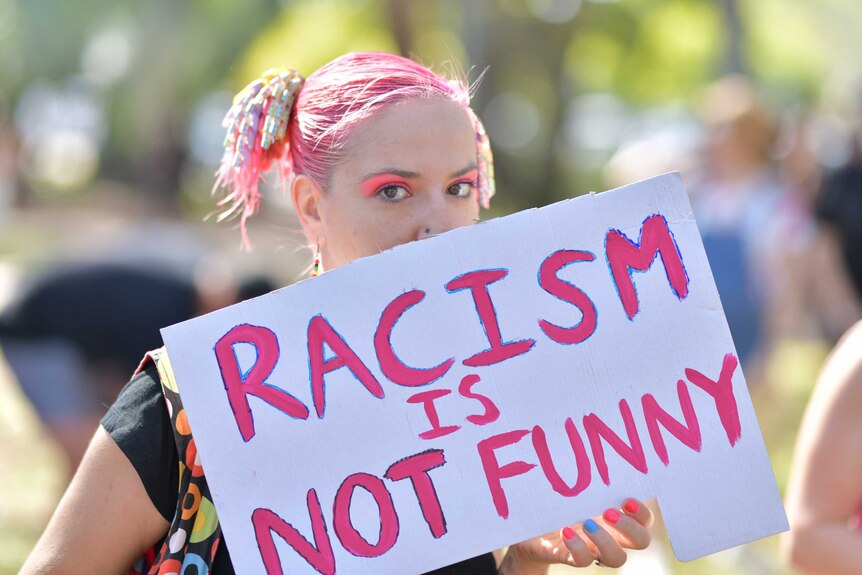 A woman holds a sign 'racism is not funny'