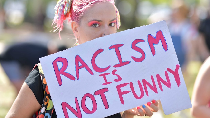 A woman holds a sign 'racism is not funny'