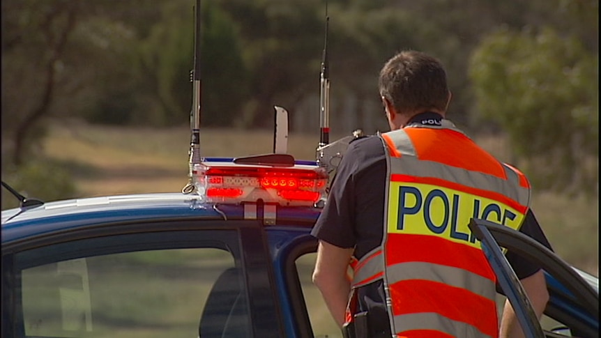 A South Australian police officer stands outside a police car.