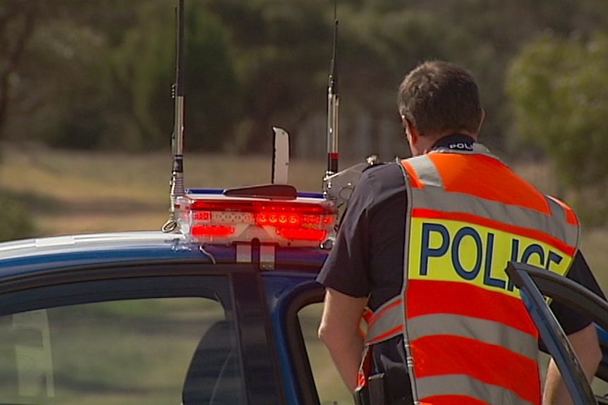 A South Australian police officer stands outside a police car.