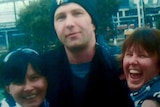 A man wearing a beanie stands in between his two sisters.