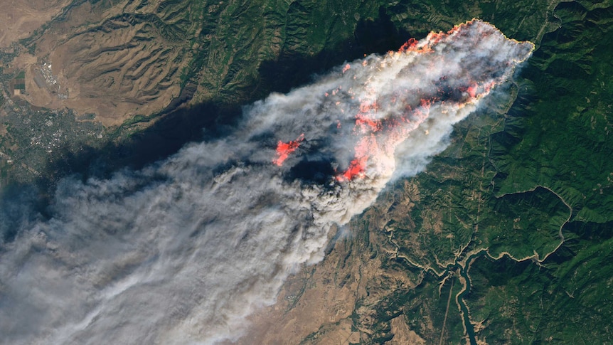 Satellite image of a section of california, showing angry red fire and smoke streaming across a strip of green land