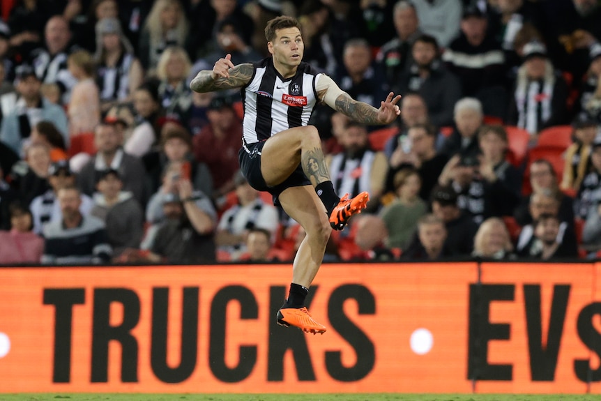 A Collingwood player is in mid-air after completing a kick for goal.