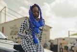 Rapper and singer-songwriter Sampa The Great leans against a car