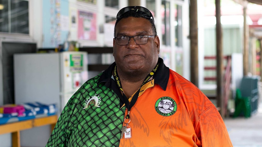 A man wearing glasses and a bright orange-and-green shirt looks at the camera.