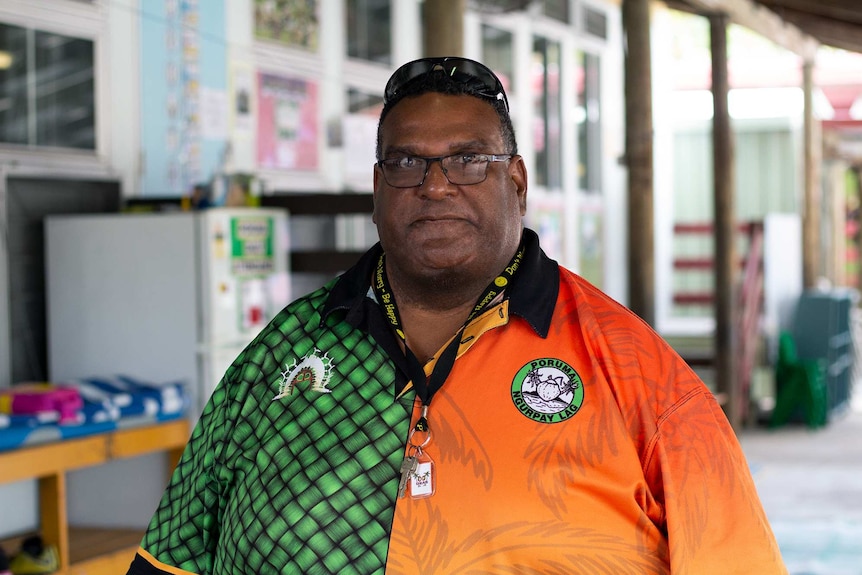 A man wearing glasses and a bright orange-and-green shirt looks at the camera.