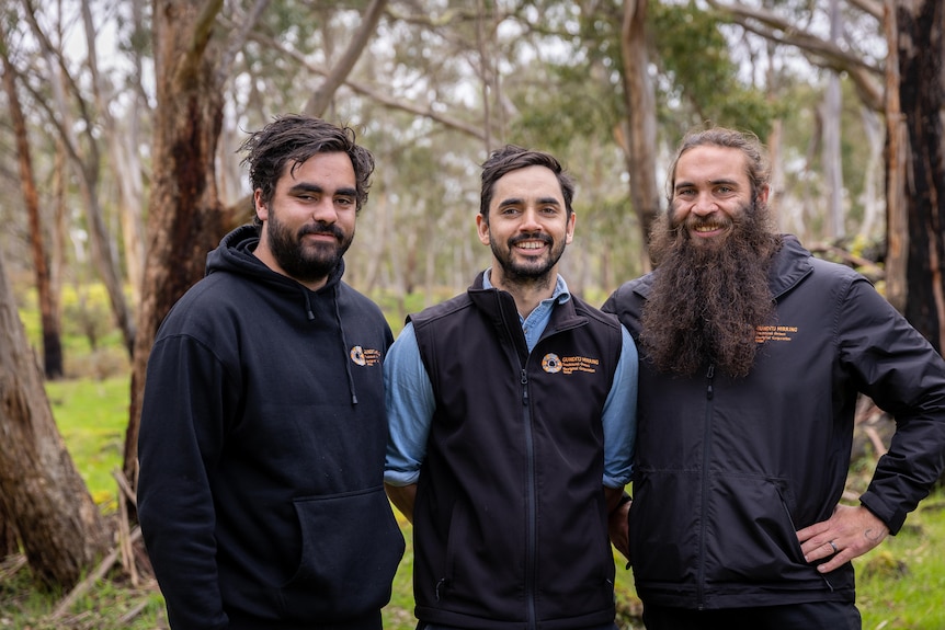 Three young Indigenous men pose for a photo in the bush.