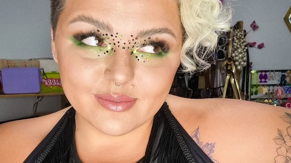 A woman wearing a black crop top, bright green eye makeup and bleached blonde hair is looking to the right side of the screen.