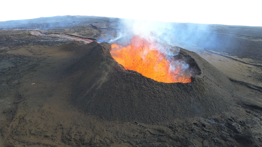Image of a large crater spewing lava. The area around it is dark and looks barren.