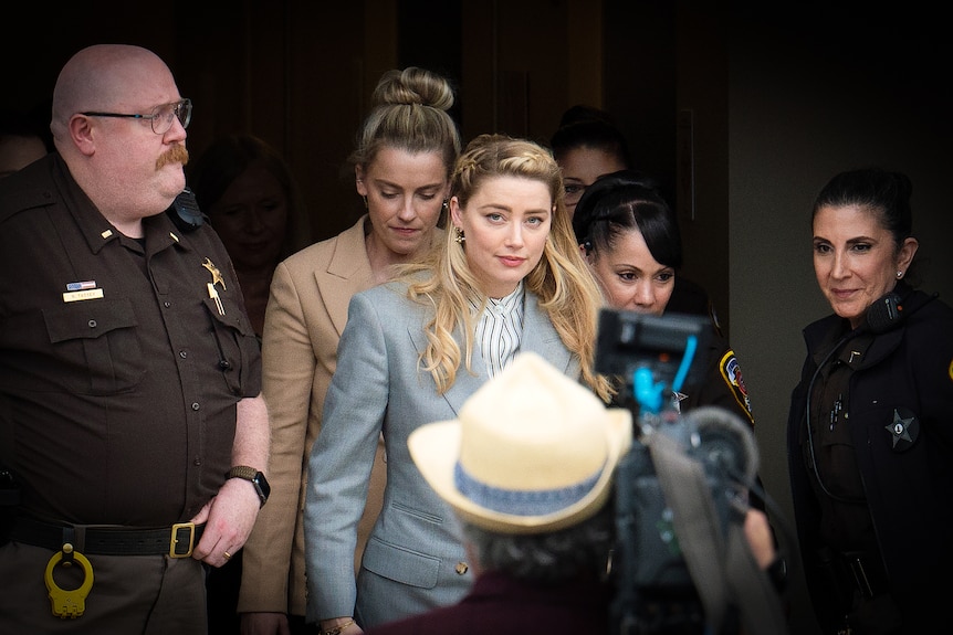 Amber Heard in a blue suit walks down a courthouse's steps surrounded by police and journalists