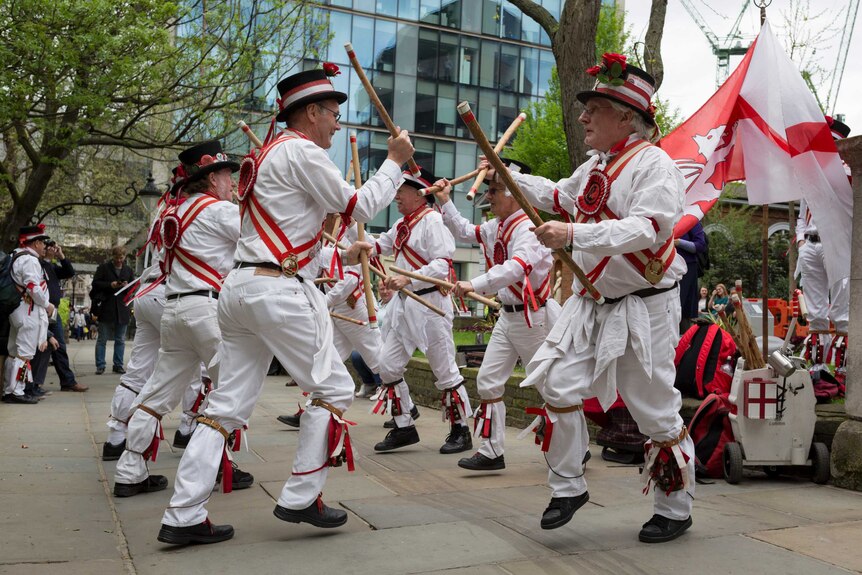 Men in dressed in the red and white of the St George's flag hold sticks are dance between each other in a line formation.