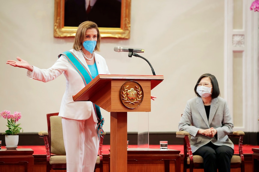 Nancy Pelosi wearing a blue ribbon behind a lectern with Tsai Ing-wen.