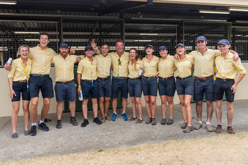 Twelve people in yellow shirt stand in a line cheering.