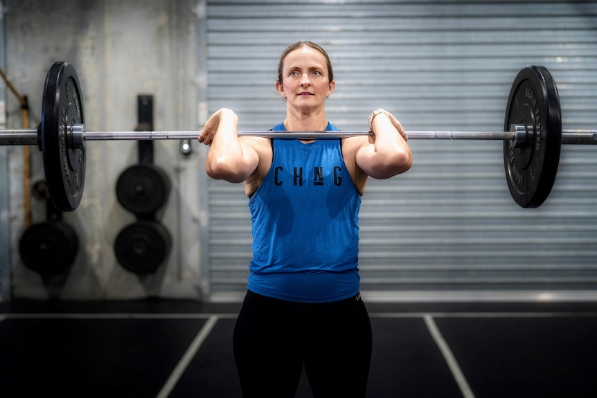 A white woman wears gym gear while lifting a dumbell at a gym