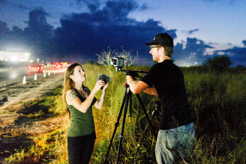 Two people set up a camera at dawn.