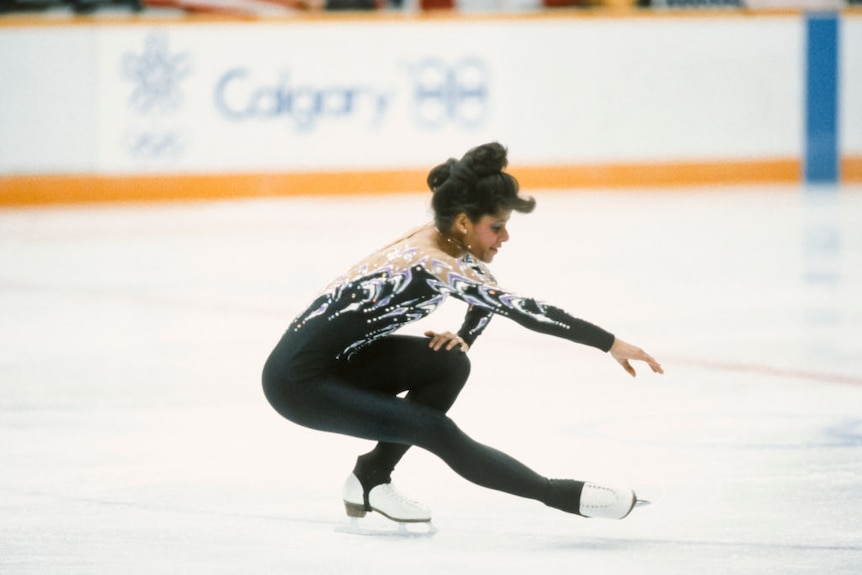 A woman wearing a black and silver leotard, figure-skating.