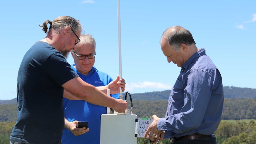 Three men work on electronic equipment.