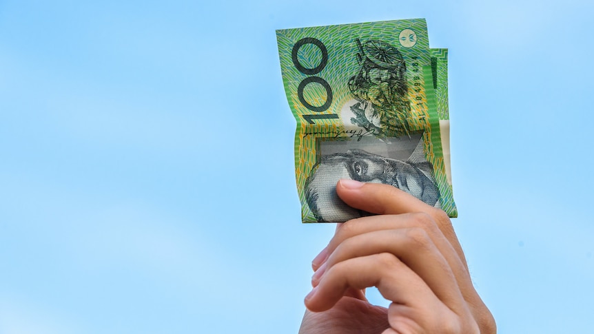 A woman's hand holding a $100 note in the air, against a blue sky.