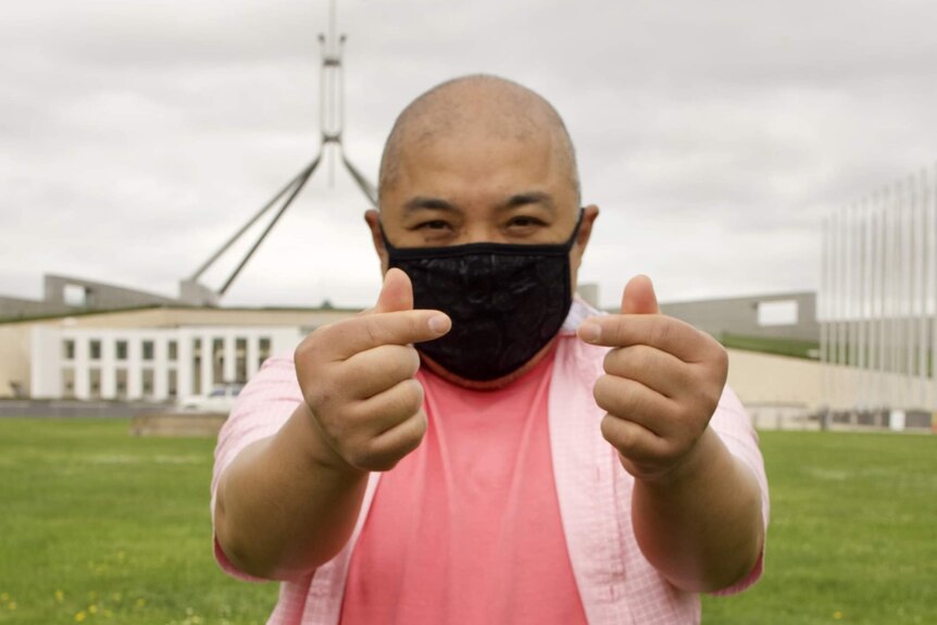 A man wearing a mask holds his thumbs up to the camera.