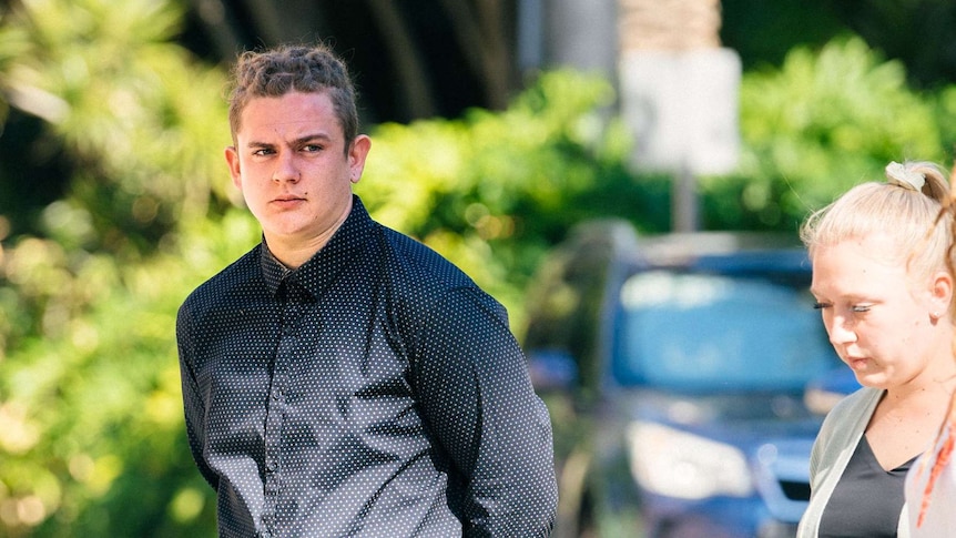 A young man with his hands behind his back walks outside