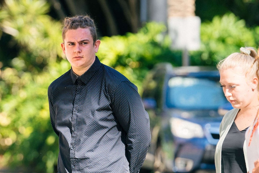 A young man with his hands behind his back walks outside