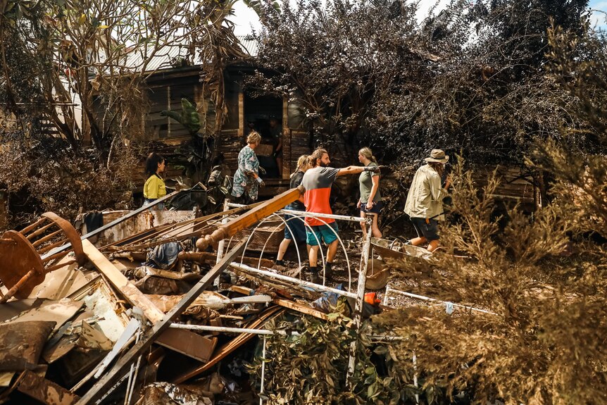 Rubble fills the yard of a wooden house as people organise themselves to clean up