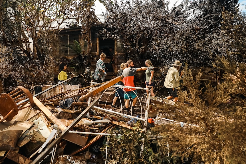 Rubble fills the yard of a wooden house as people organise themselves to clean up
