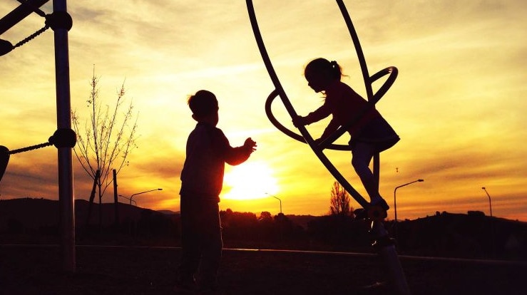 Two children playing in a play ground at sunset