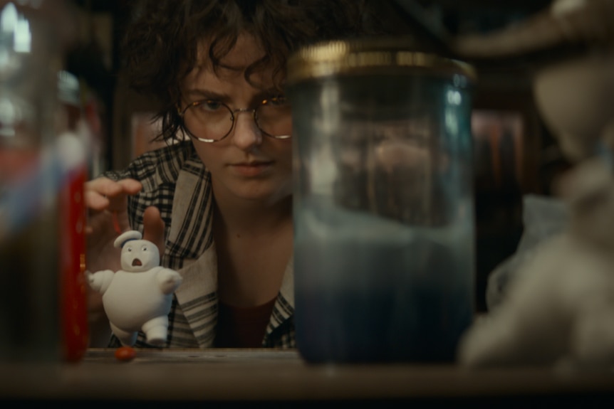 A woman looks at a small Stay Puft marshmallow men through glass jars.