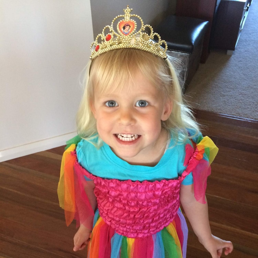 Monique Squires looks at the camera and smiles wearing a rainbow dress and tiara.