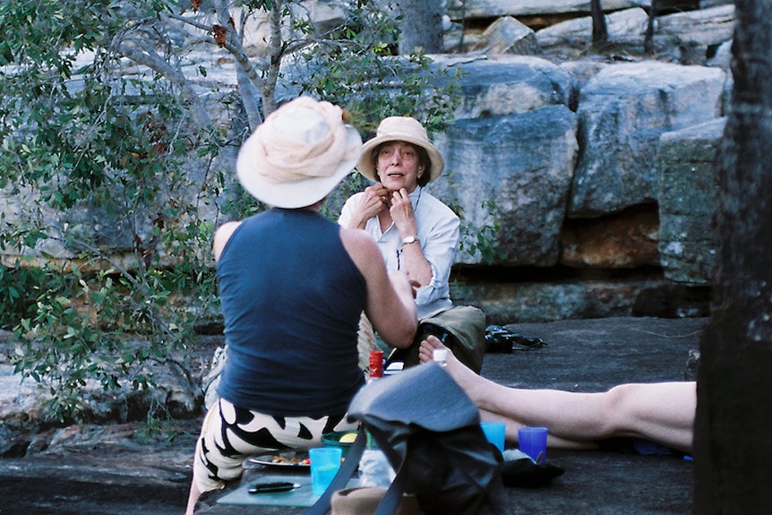 Cummings sits facing another woman in an outback setting.