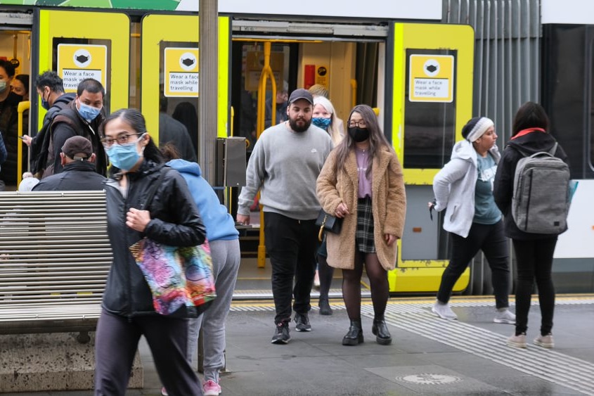 People disembarking a tram in Melbourne, many of whom are wearing masks.