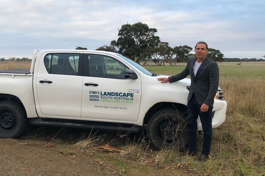 A man standing in a field next to a Landscape Board vehicle.