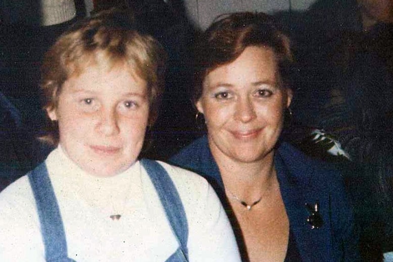 A mother and daughter sit close together looking at the camera.