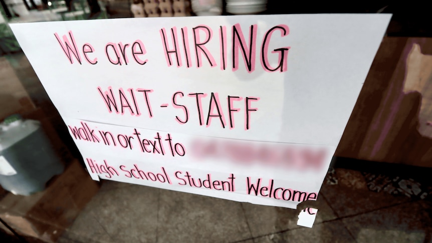 A sign saying "we are hiring" displayed in a cafe window.