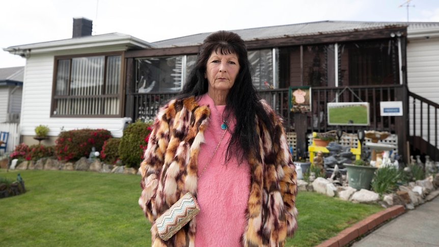 A middle aged woman stands outside a house