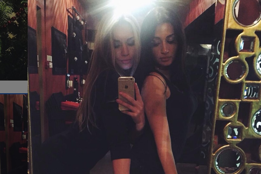 Maria and a friend take a photo in a mirror.