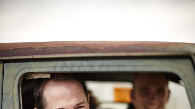 A close shot of a smiling Brett McClen, looking through driver's seat window of a rusted four wheel drive.