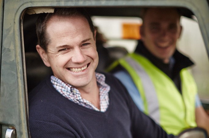 A close shot of a smiling Brett McClen, looking through driver's seat window of a rusted four wheel drive.