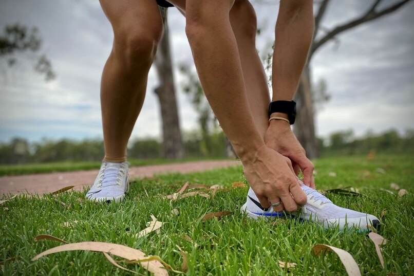 A picture of a person bending down to tie their running shoes in a park.