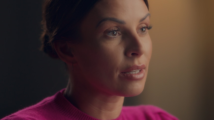A woman with brown hair and a pink jumper looks off to the side 
