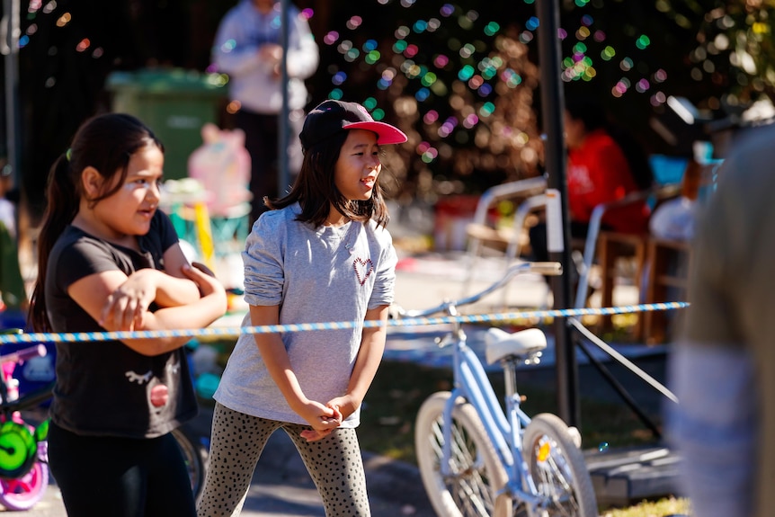 An image of two youth waiting for the ball as they play volleyball in front of a gazebo, bike, toys on a suburban street