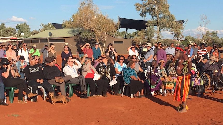 A crowd of people sit in the sun as the statement on Indigenous recognition in the constitution is read.