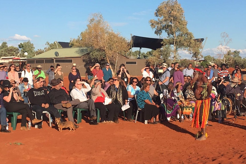 A crowd of people sit in the sun as the statement on Indigenous recognition in the constitution is read.