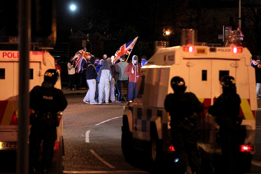 Police stand guard as protesters wave the Union flag during clashes in Belfast, Northern Ireland.
