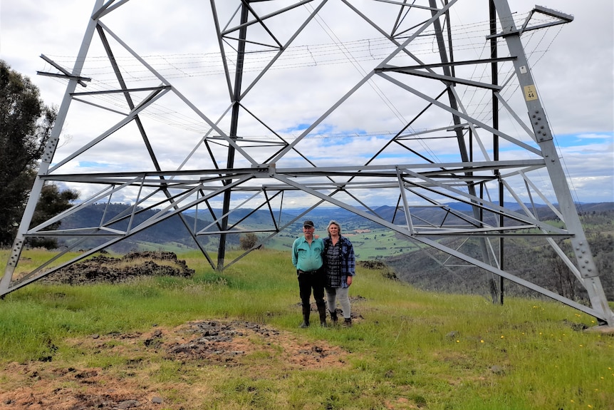 A man and a woman stand under a metal structure with a green valley behind them.