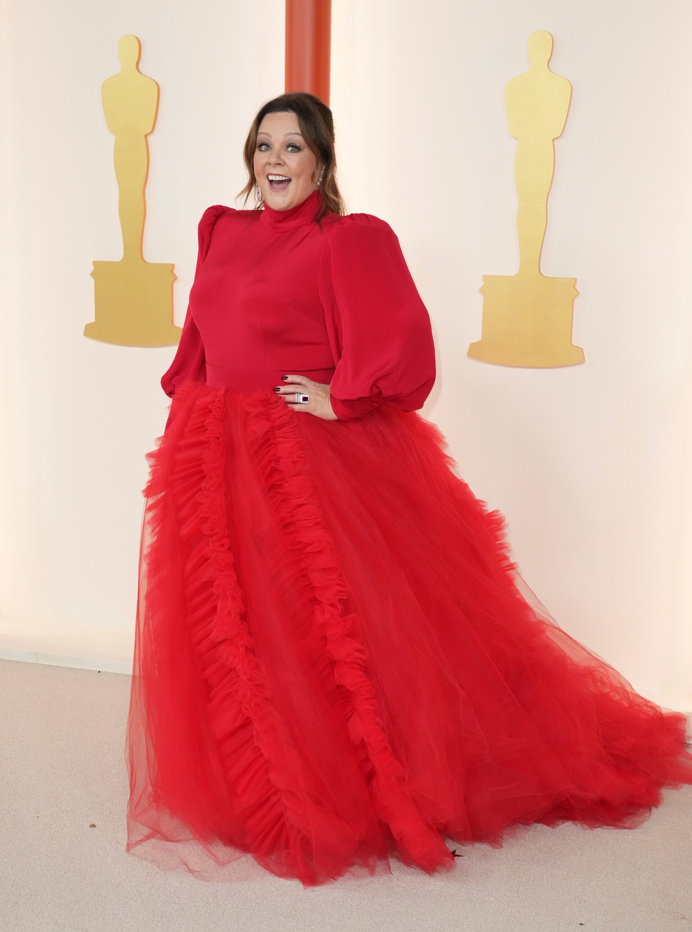 Melissa McCarthy wearing a long-sleeved, full-length red gown with a tulle ruffled skirt.