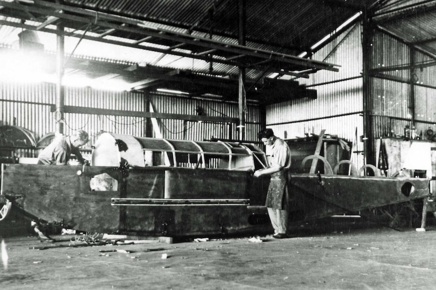 A black and white archive photo of two men building a small aeroplane in a hangar.